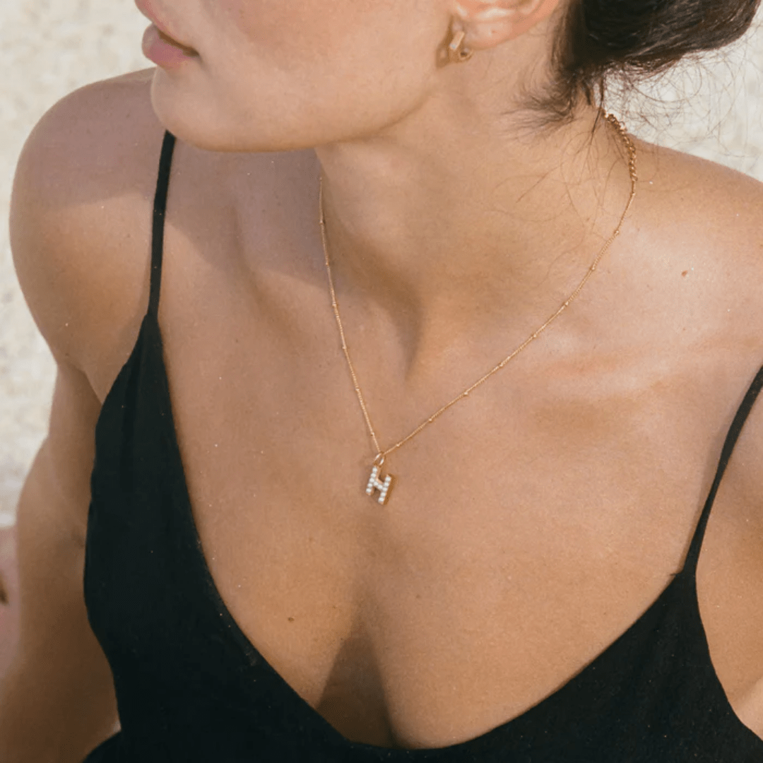 Gold necklace with letter H pendant worn on beach outfit – Moonela Jewelry